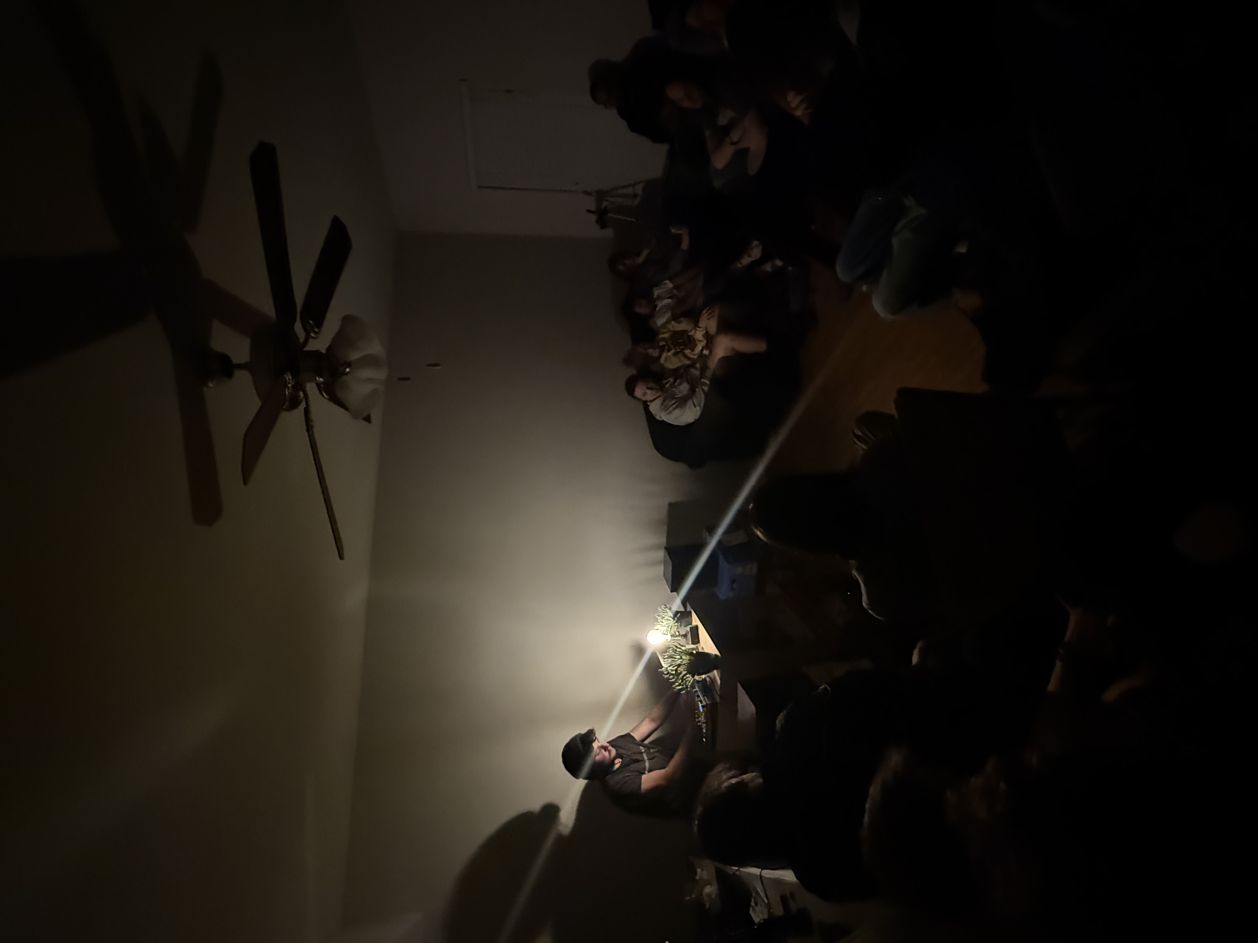 The artist performing Synonyms of a Person beside a lamp and seated audience